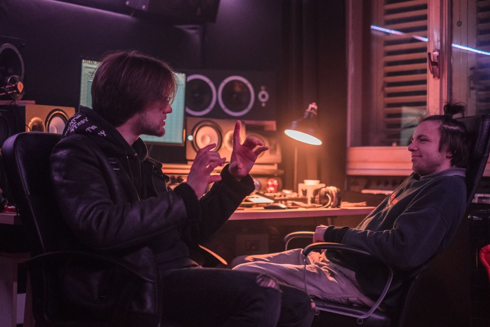 Two music professionals talk beside recording equipment in a studio