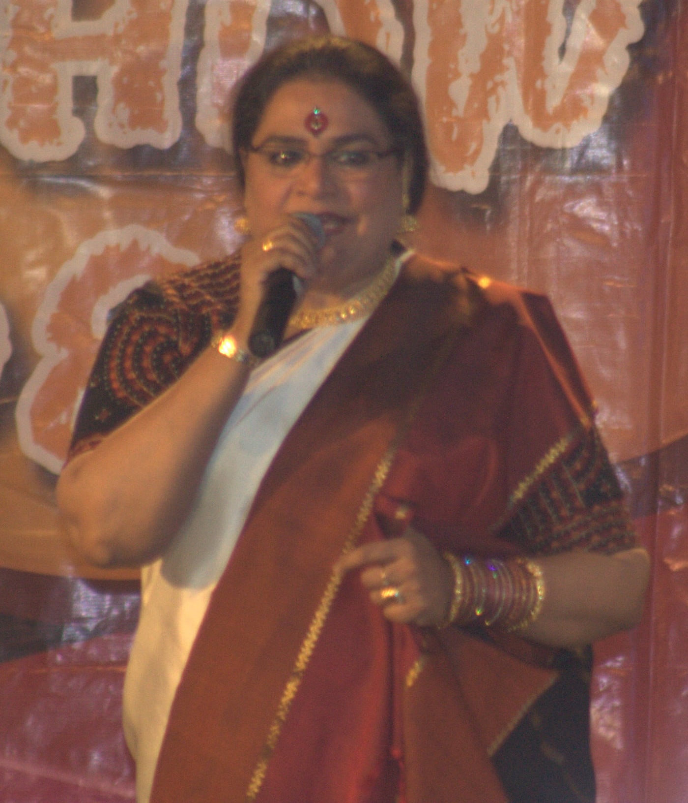 Usha Uthup singing into a microphone while wearing a saree on stage