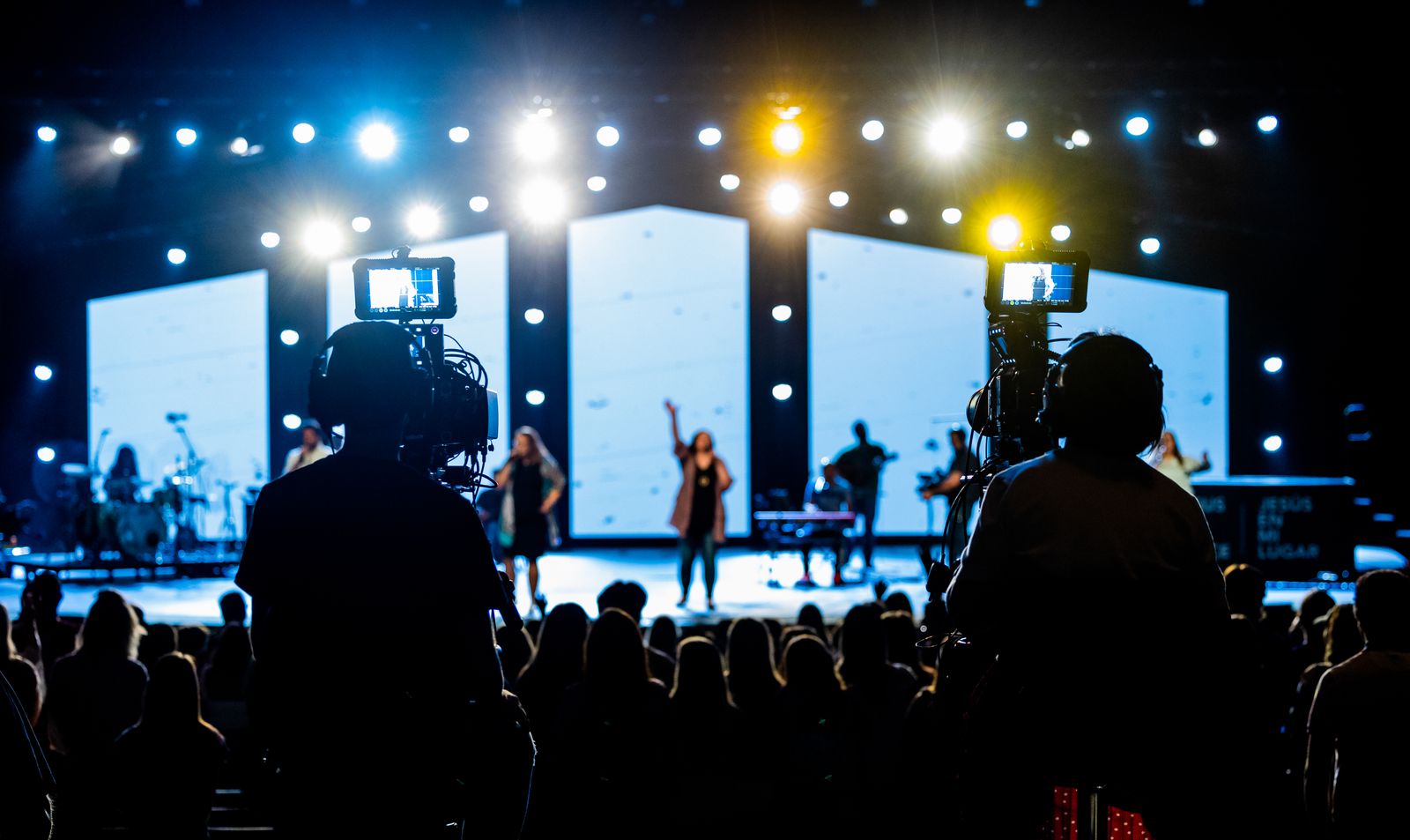 Two camera operators record a live performance from the audience area
