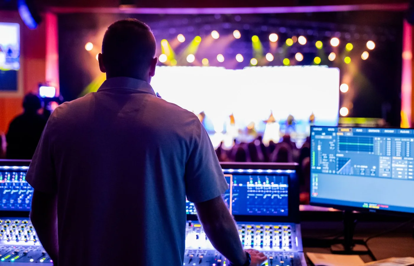 A concert audio engineer working at a mixing desk with the stage in view