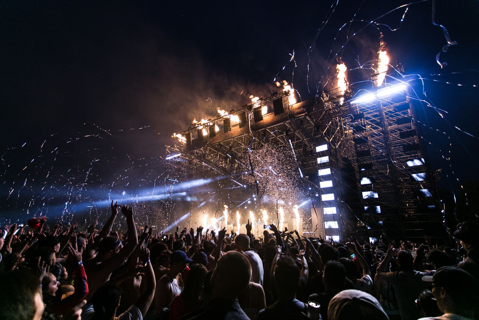 A large live-music crowd facing a stage with lights and pyrotechnics