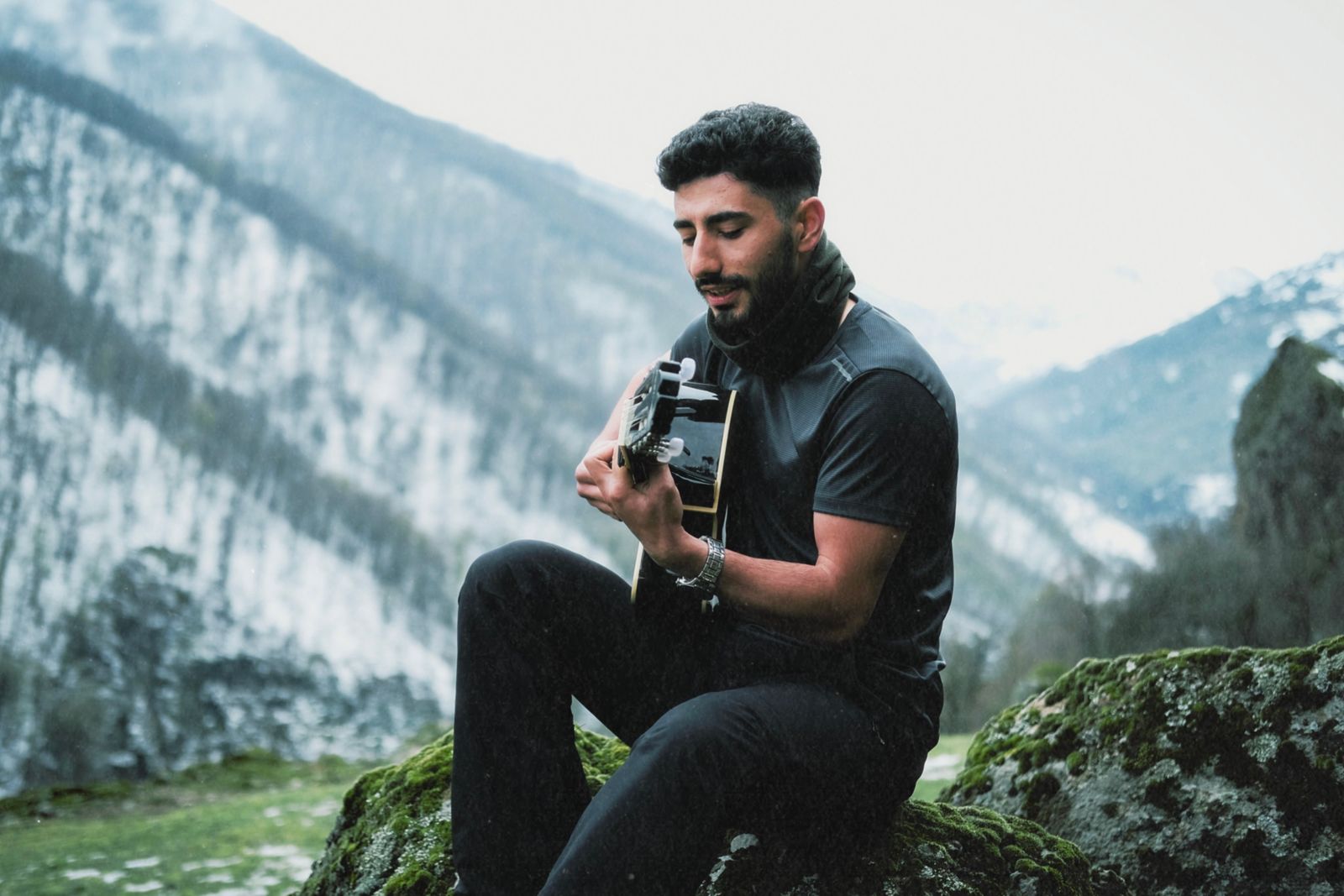 A guitarist playing an acoustic guitar among snow-covered mountains